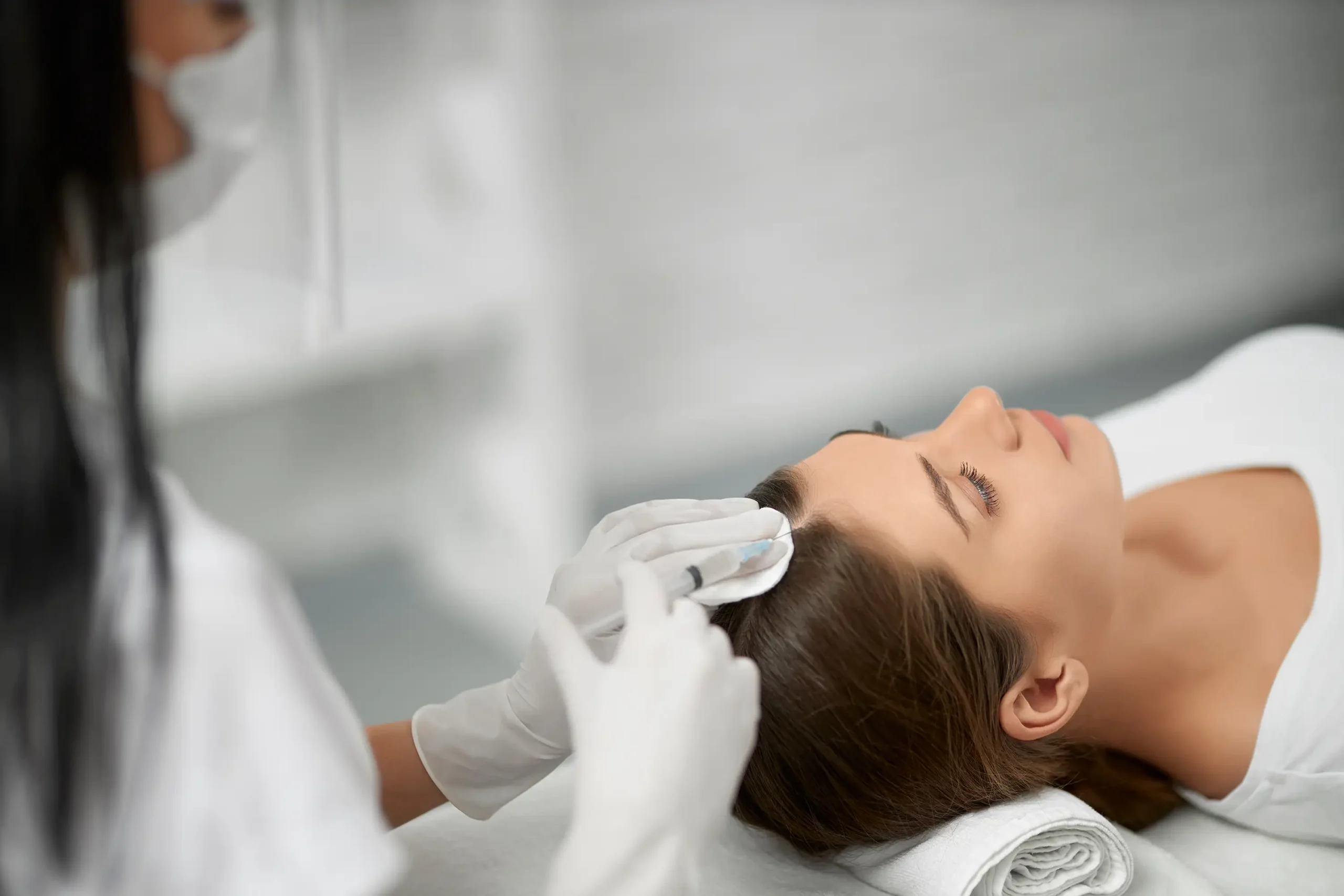 Aplikácia Regenera Activa na pokožku hlavy u ženy počas ošetrenia v klinike